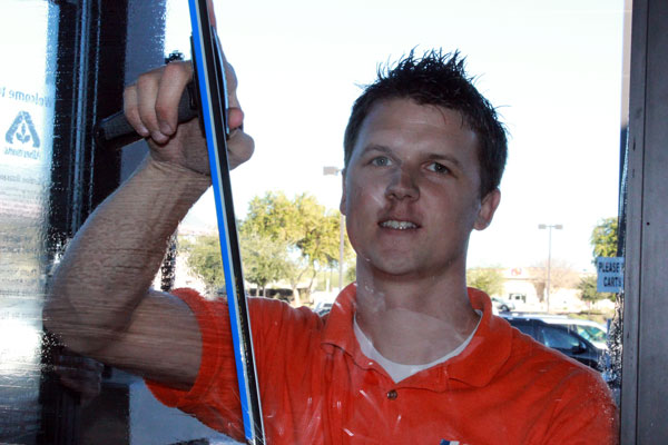 A window cleaner smiling while cleaning a grocery store window.